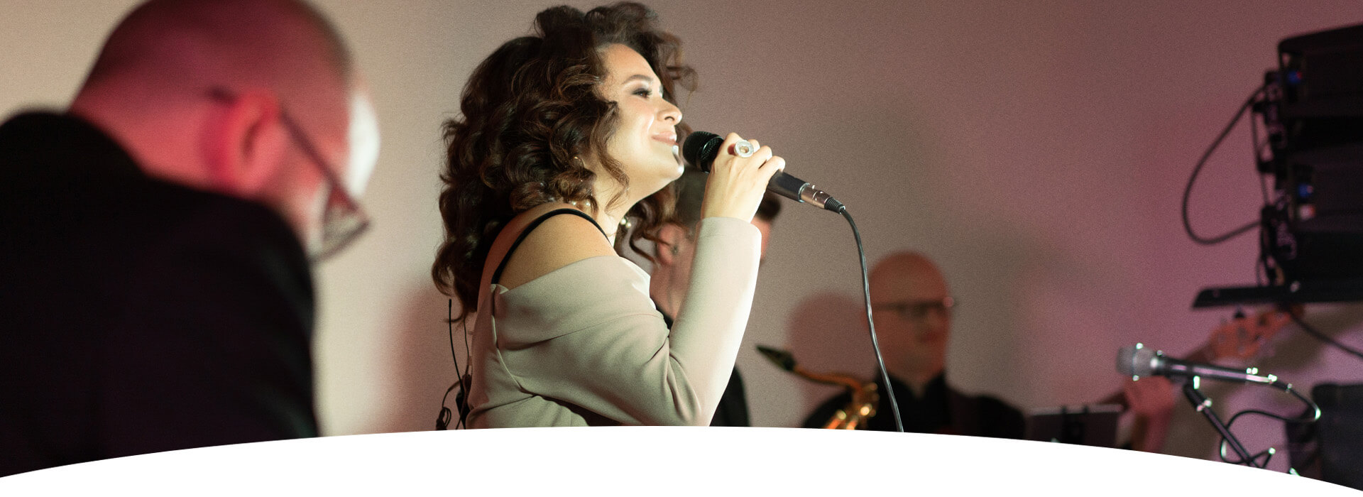 eine braunhaarige Sänger mit einem Mikrofon und ihrer Band im Hintergrund